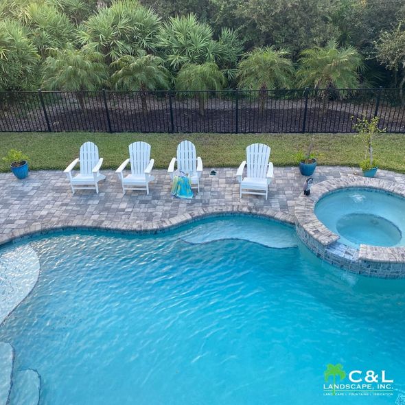 Pool with white Adirondack chairs, a hot tub, and a black fence in the backyard.