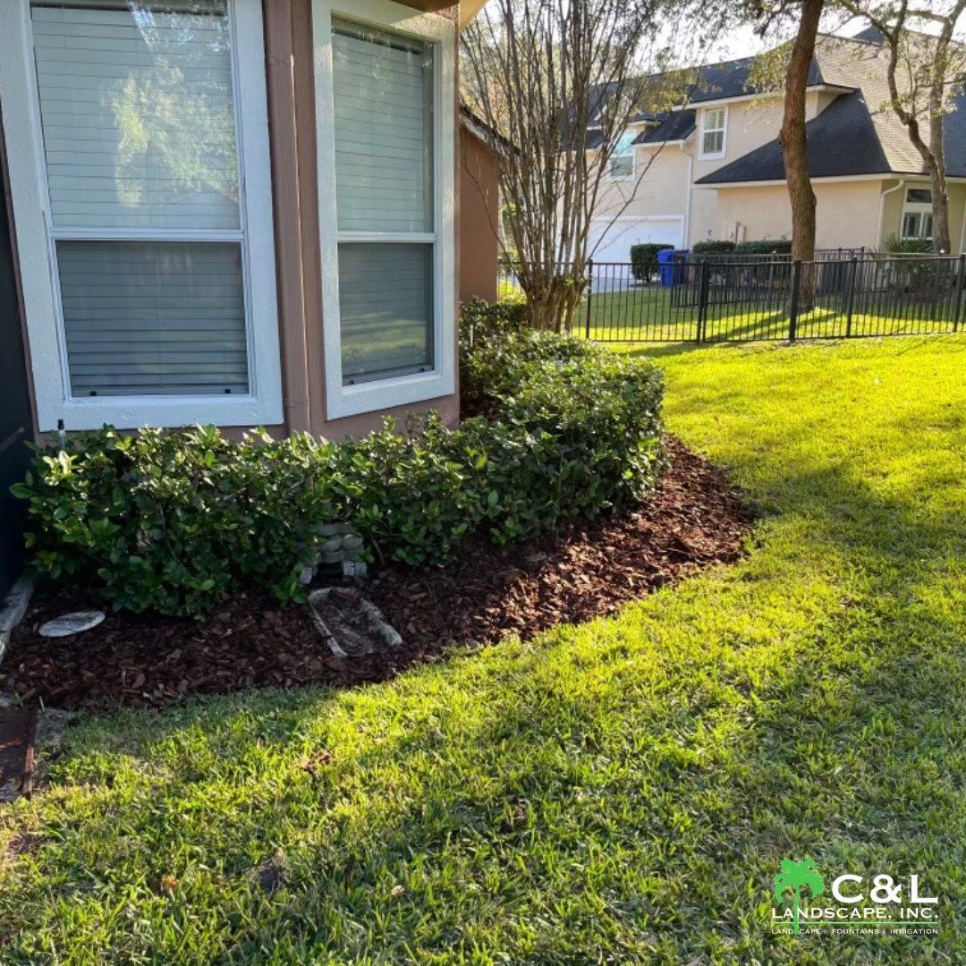Corner of a house with windows, a mulched garden, and a grassy lawn.