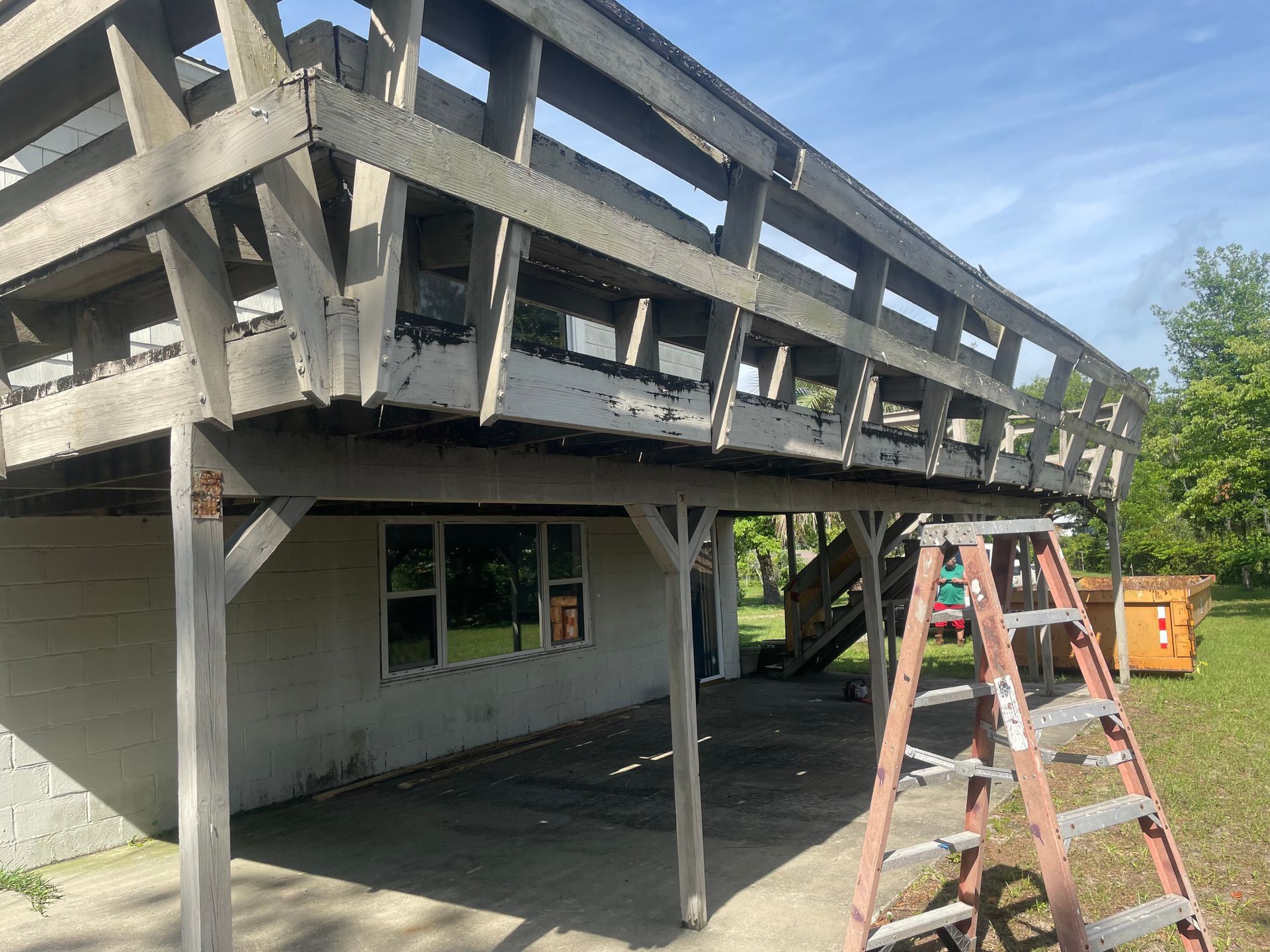 Wooden deck over a concrete structure with a ladder and dumpster in view.