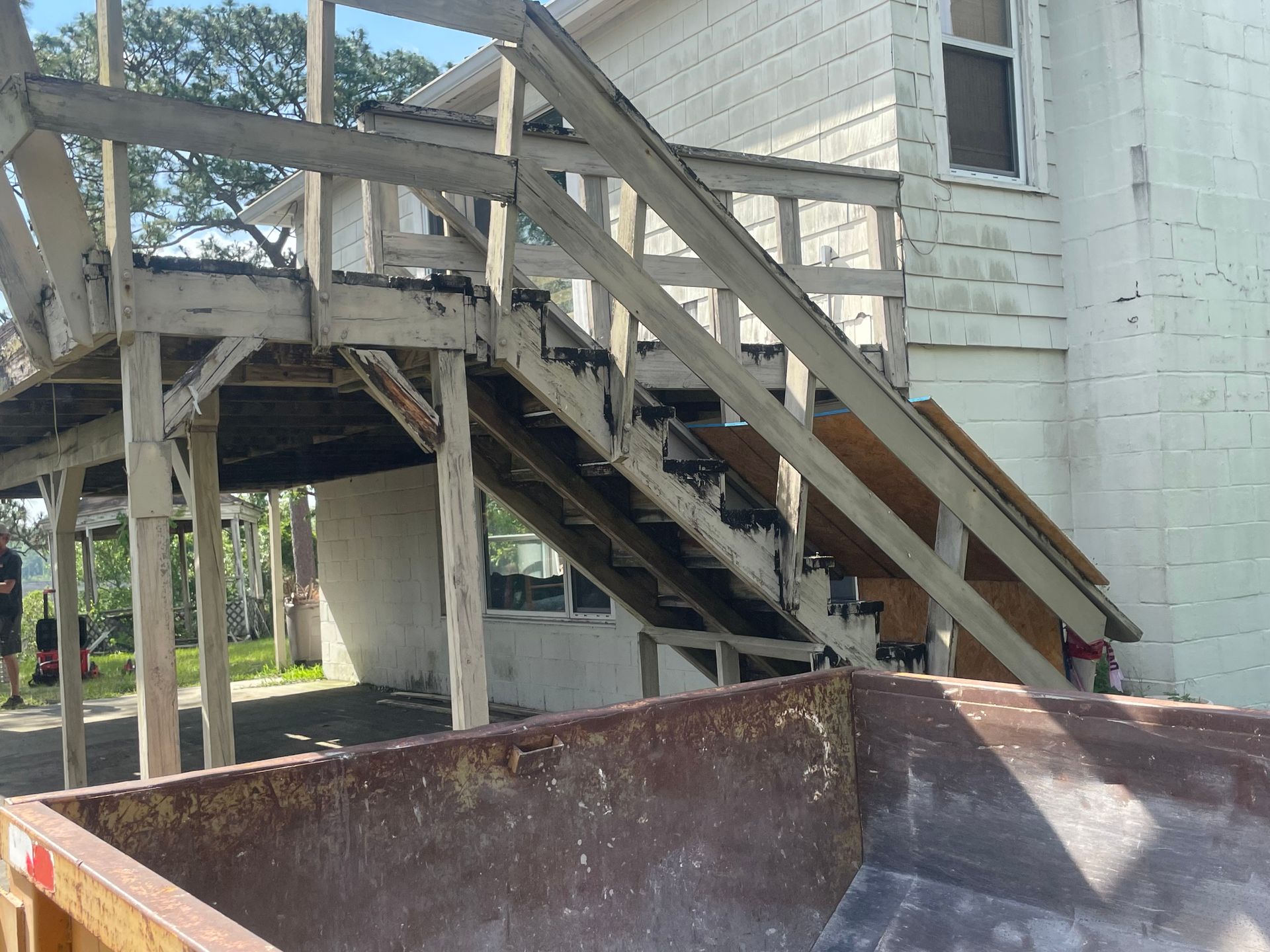Dilapidated exterior staircase next to a white building; a dumpster sits in front of it.