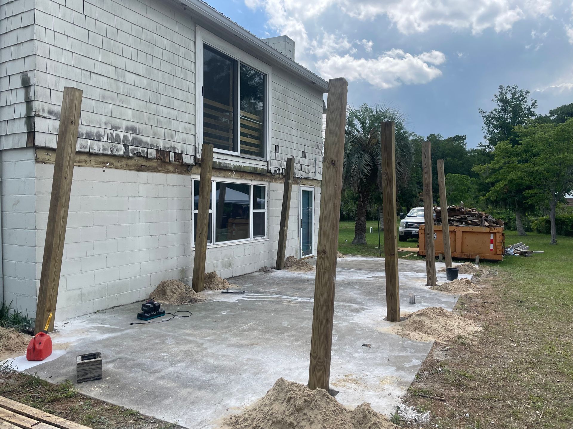 Construction site: Exterior of a house with concrete patio, wooden posts, and construction materials.