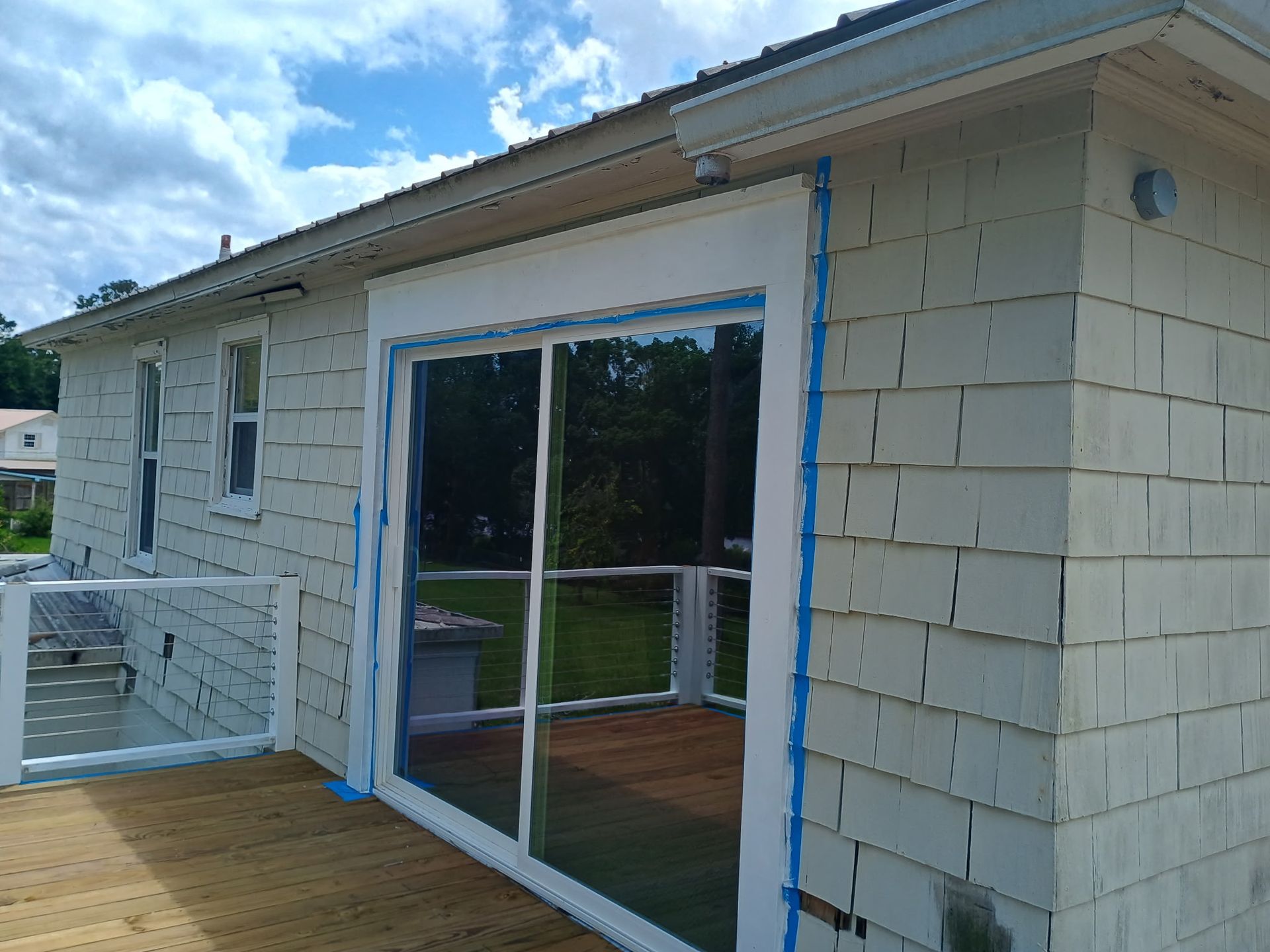 Exterior view of a house with white siding and a sliding glass door; blue tape outlines the door frame.