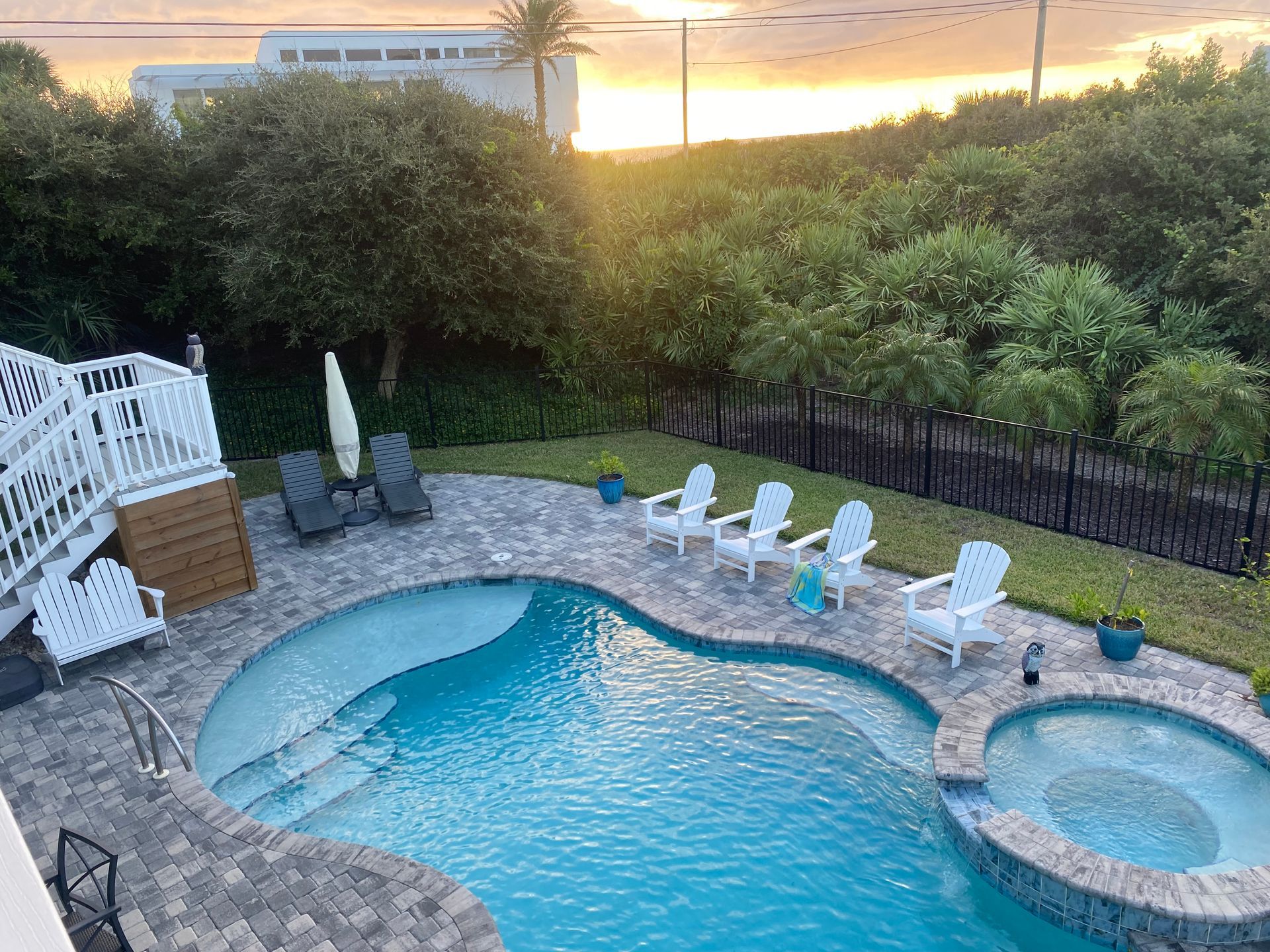 Pool area with white chairs, ocean view, and sunset.