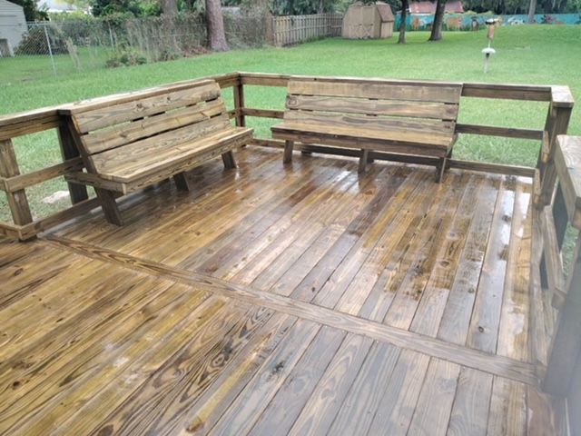 Wooden deck with two benches, railing, wet from rain, in a backyard.