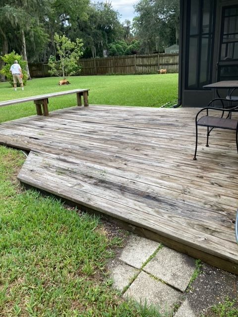 Weathered wooden deck with detached section. Green lawn surrounds it, person in background.