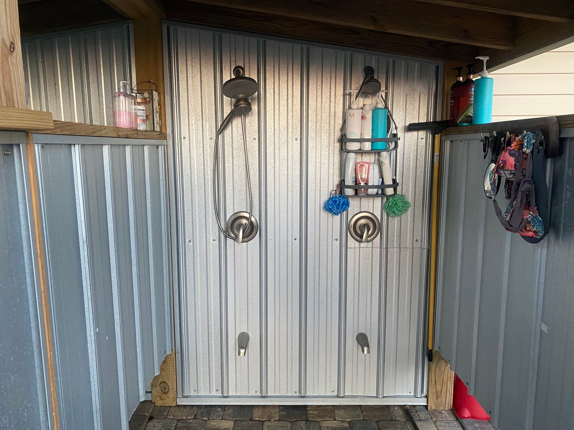 Outdoor shower with corrugated metal walls and two showerheads.