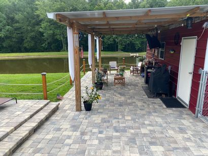 Patio with seating, a grill, and a covered area, next to a pond, in a rural setting.