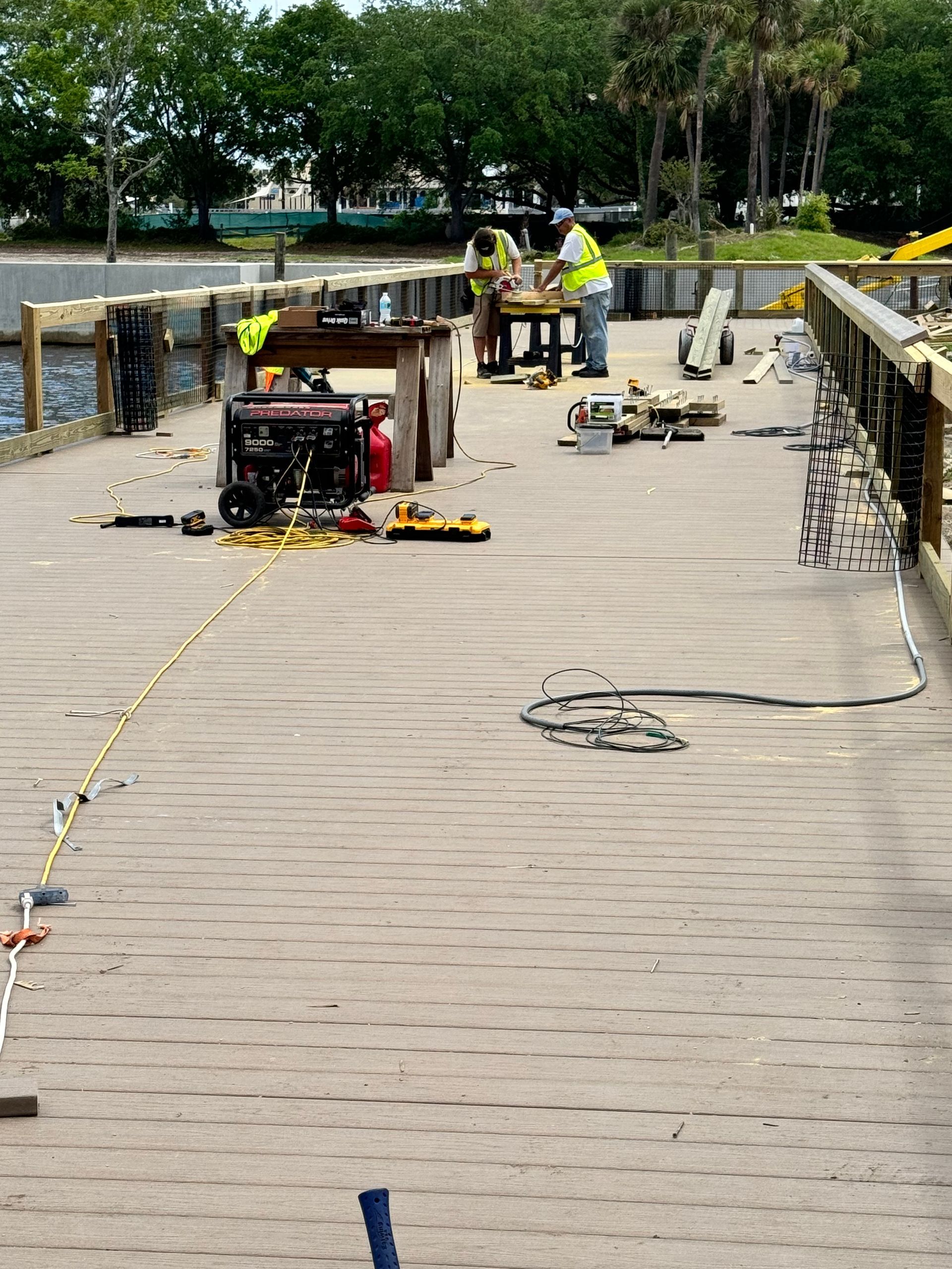 Workers building a wooden boardwalk; tools and generator on the deck.