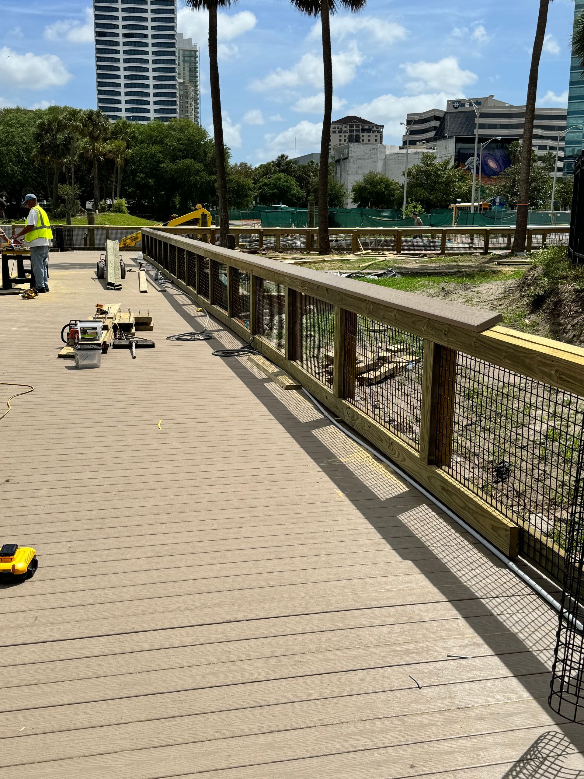 Construction site: wooden bridge with railing, tools scattered, worker in safety vest.