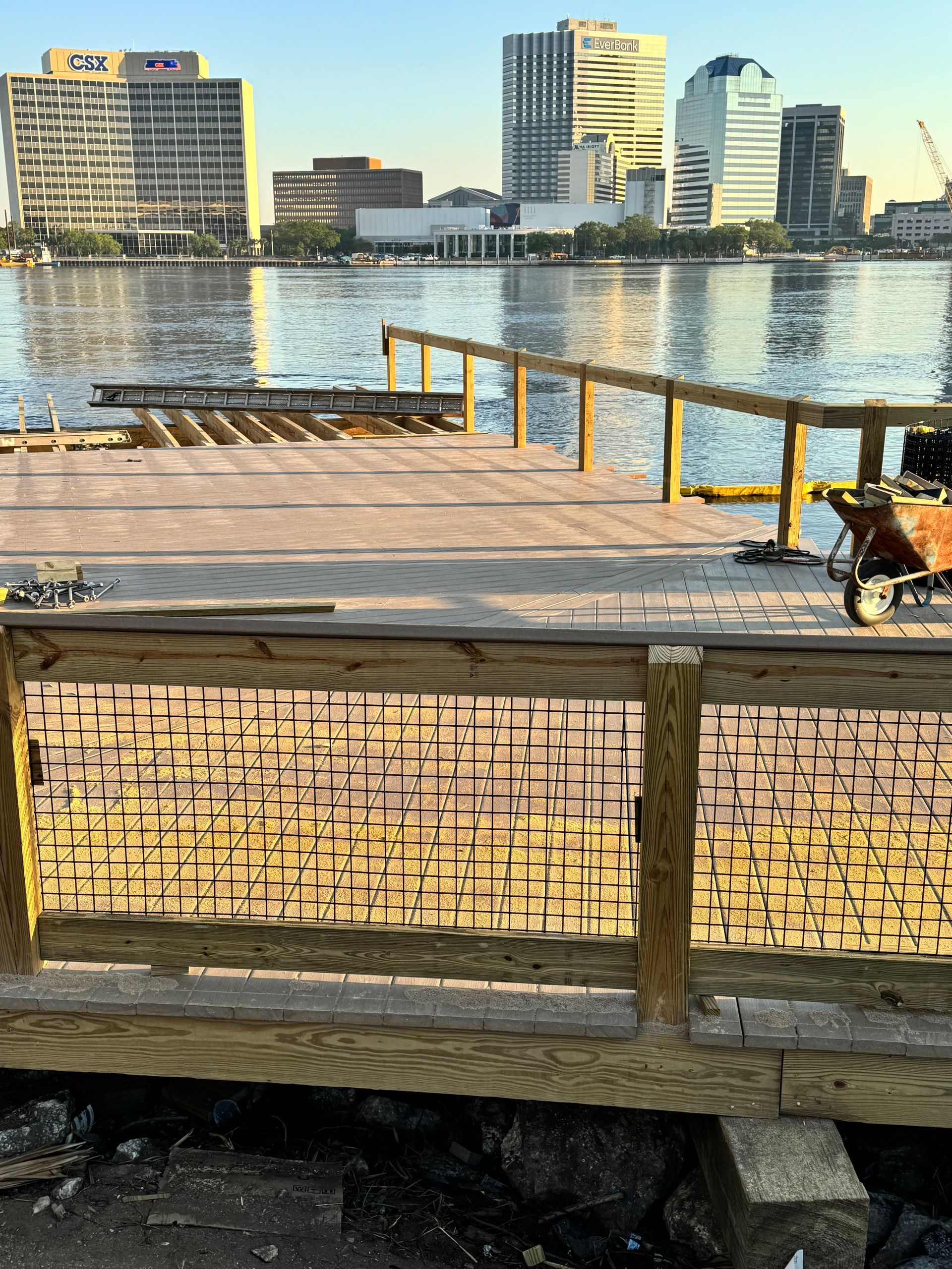 Wooden pier overlooking water with city skyline in the background. Construction materials and tools visible.
