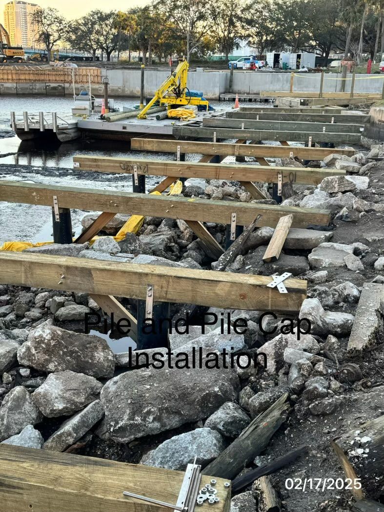 Construction site with wooden beams and rocks near water. Pile and pile cap installation.