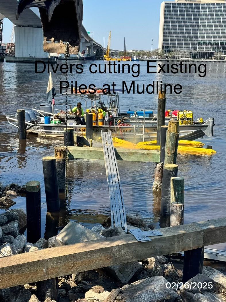 Divers cutting existing piles at mudline, boat on water. Bridge in background.