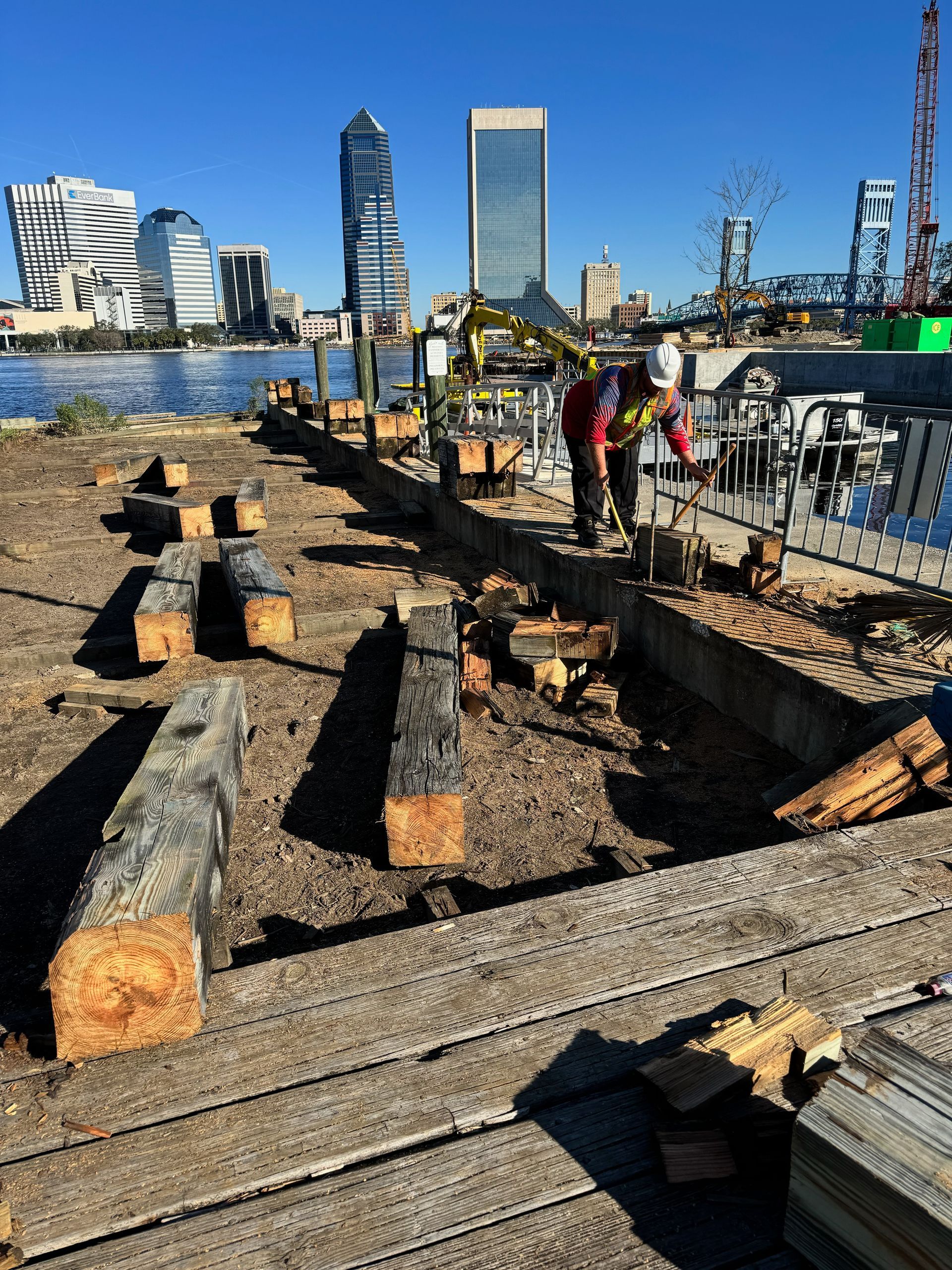 Construction site with workers, wooden beams, and Jacksonville, FL skyline in the background.