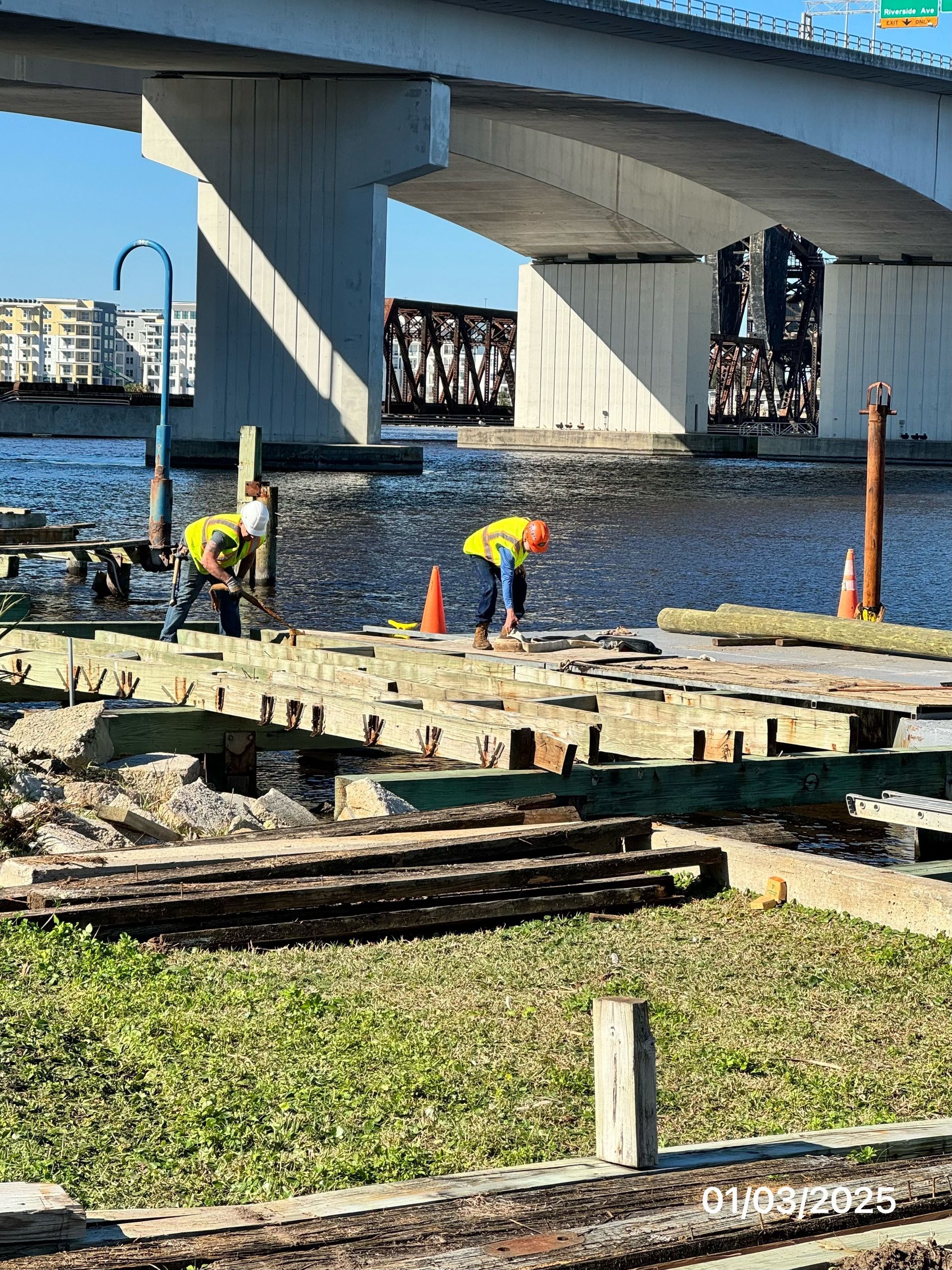 Construction workers on a dock under a bridge, wearing safety vests.