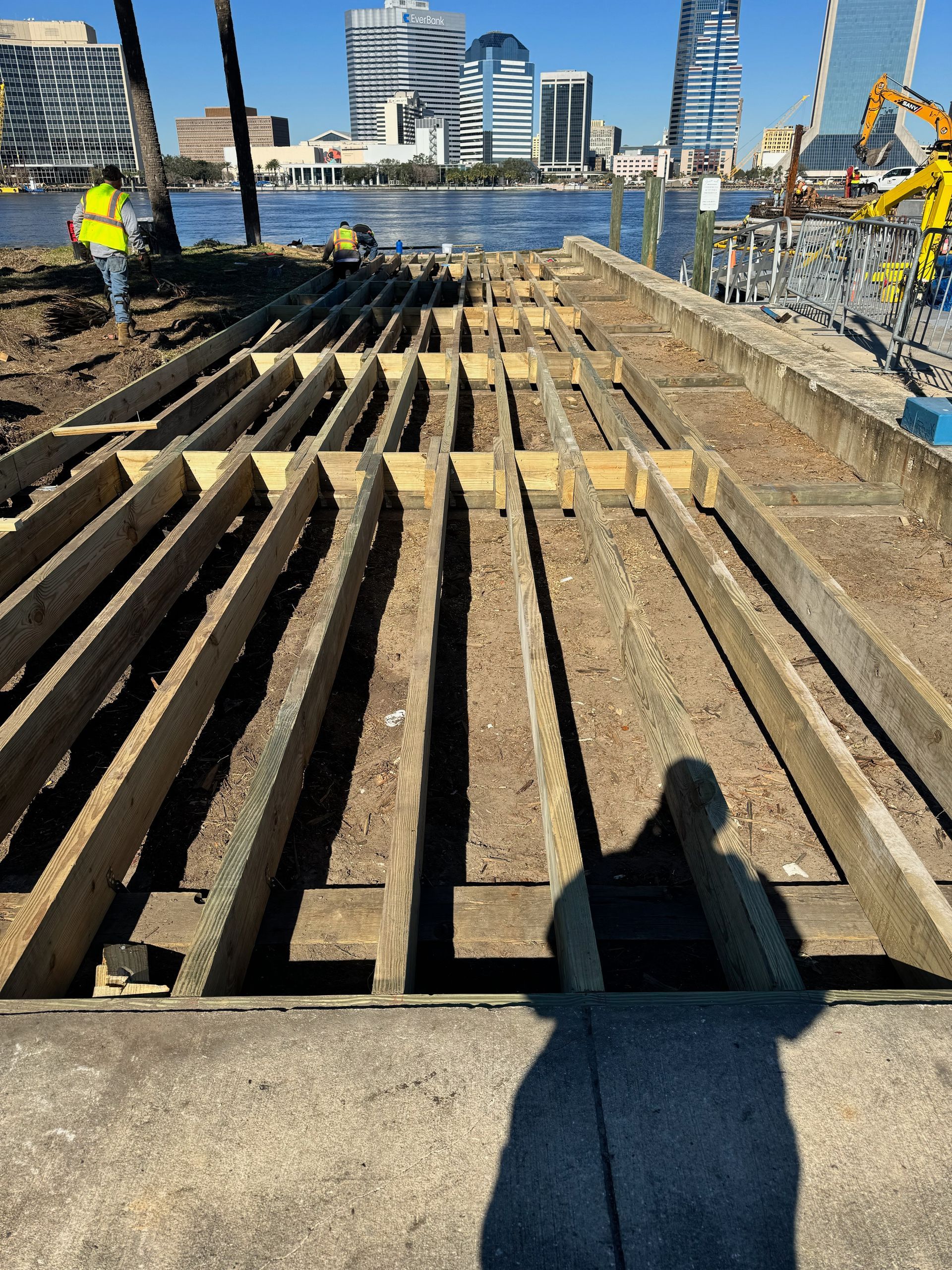 Deconstructed boardwalk with exposed wooden beams, city skyline in background, person working.