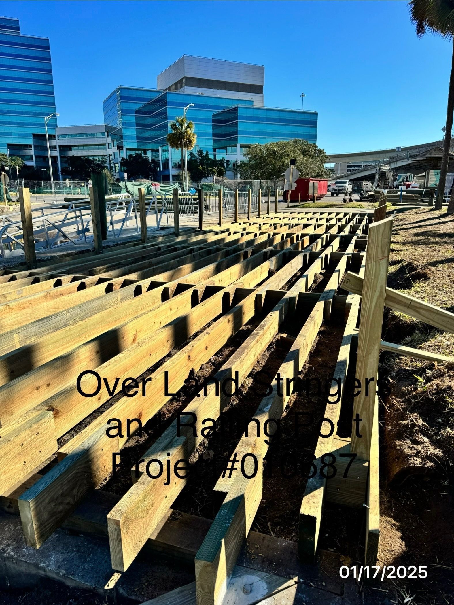 Construction site with wooden beams; multi-story buildings in background. Project #087, 01/17/2025.