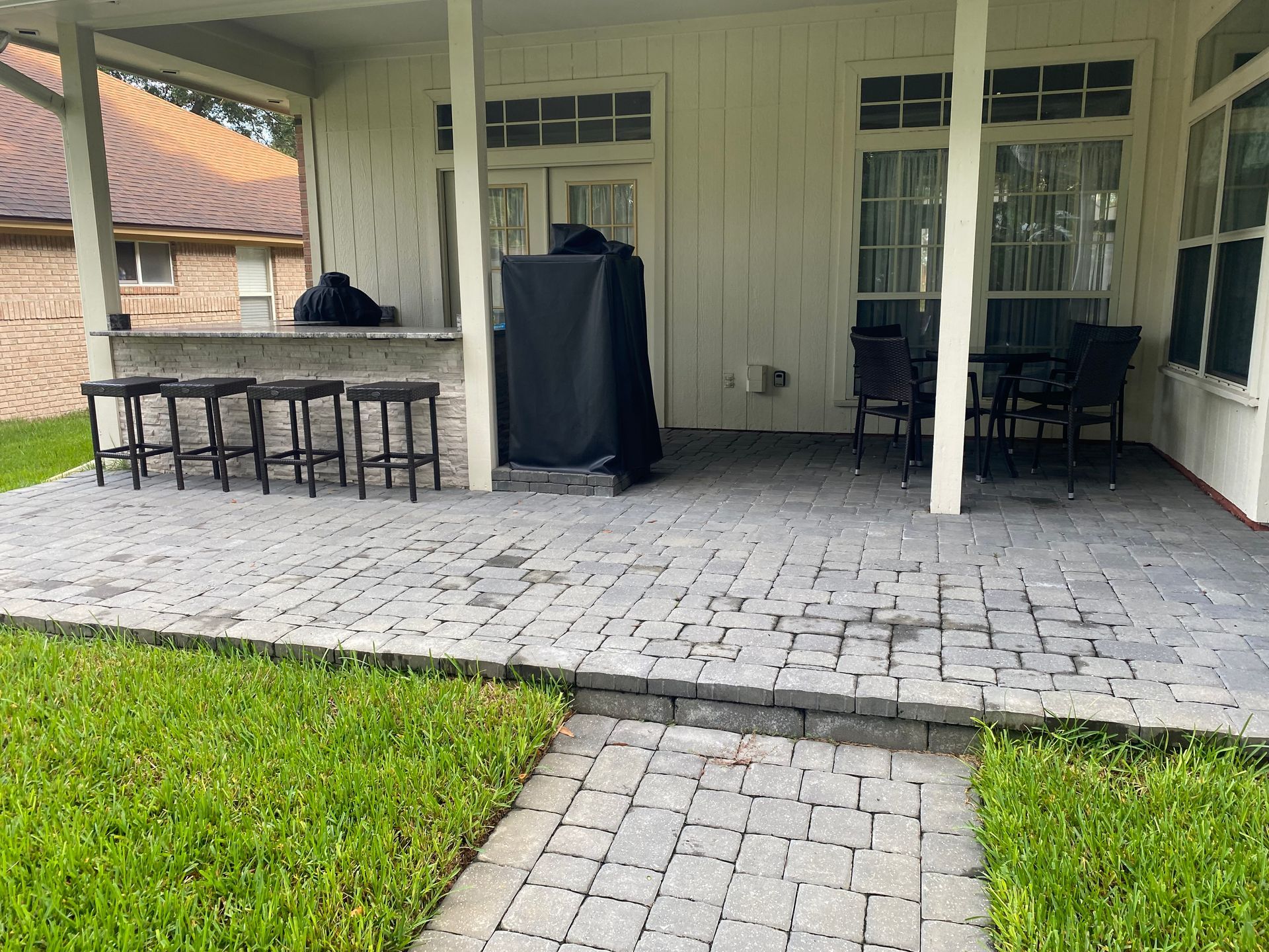 Patio with brick pavers, bar with stools, grill, and outdoor dining set.