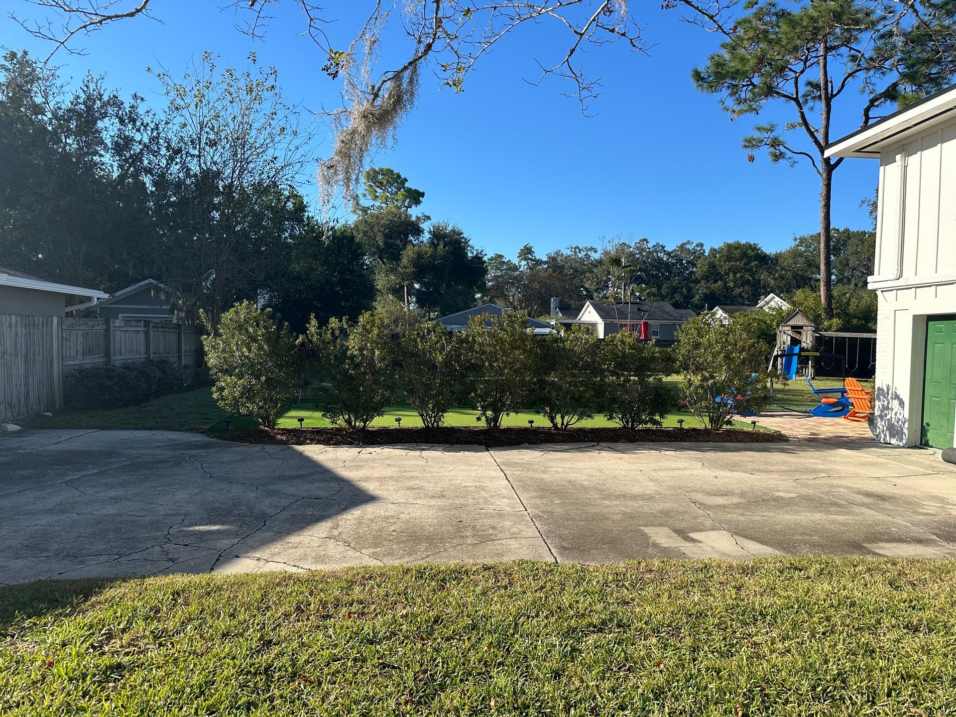 A concrete driveway in front of a trimmed hedge with a blue sky background.