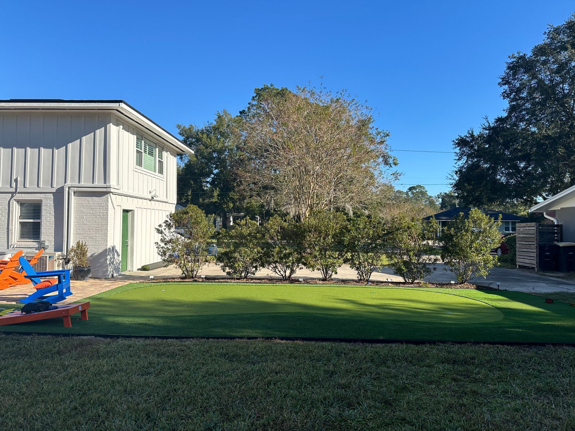 A backyard with a green lawn, shrubs, and a two-story building on a sunny day.