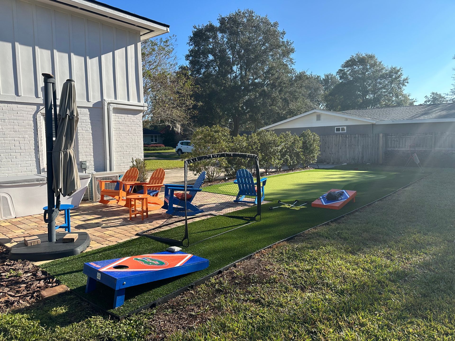 Backyard with Adirondack chairs, bean bag toss, umbrella, and a swing set on a sunny day.