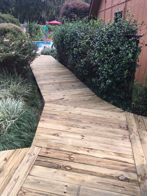 Wooden walkway alongside greenery and a building leads to a pool.