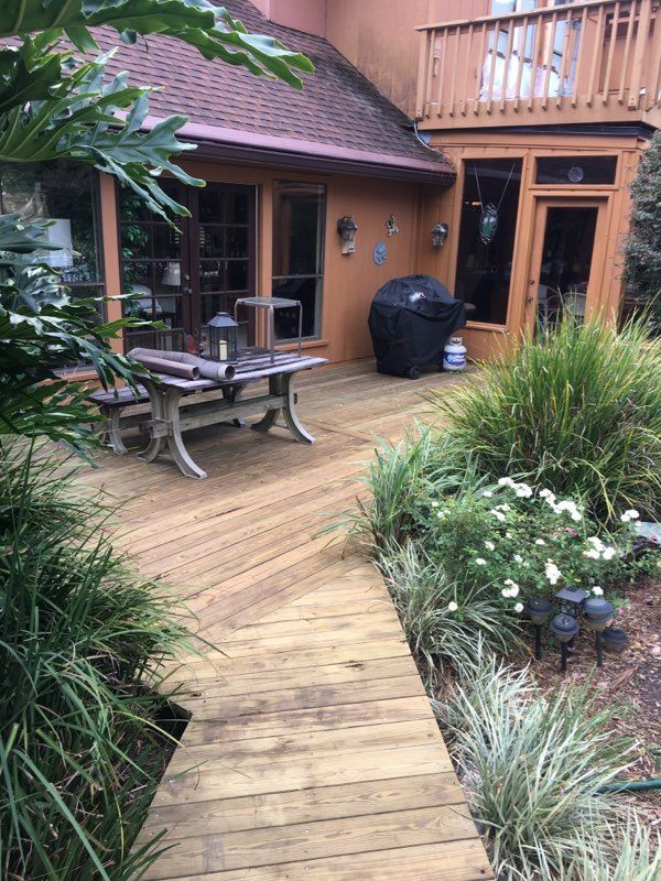 Wooden deck with table and grill next to a building. Plants surround the deck.