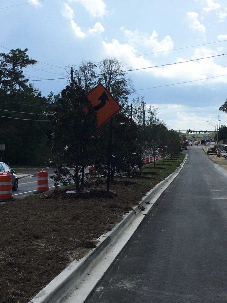 Orange curved arrow warning sign along a newly paved road.