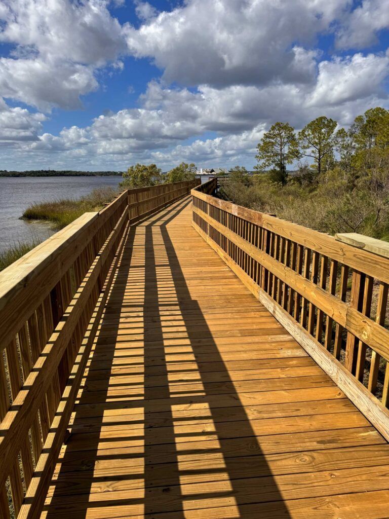 Wooden boardwalk along a marsh, under a blue sky with clouds.