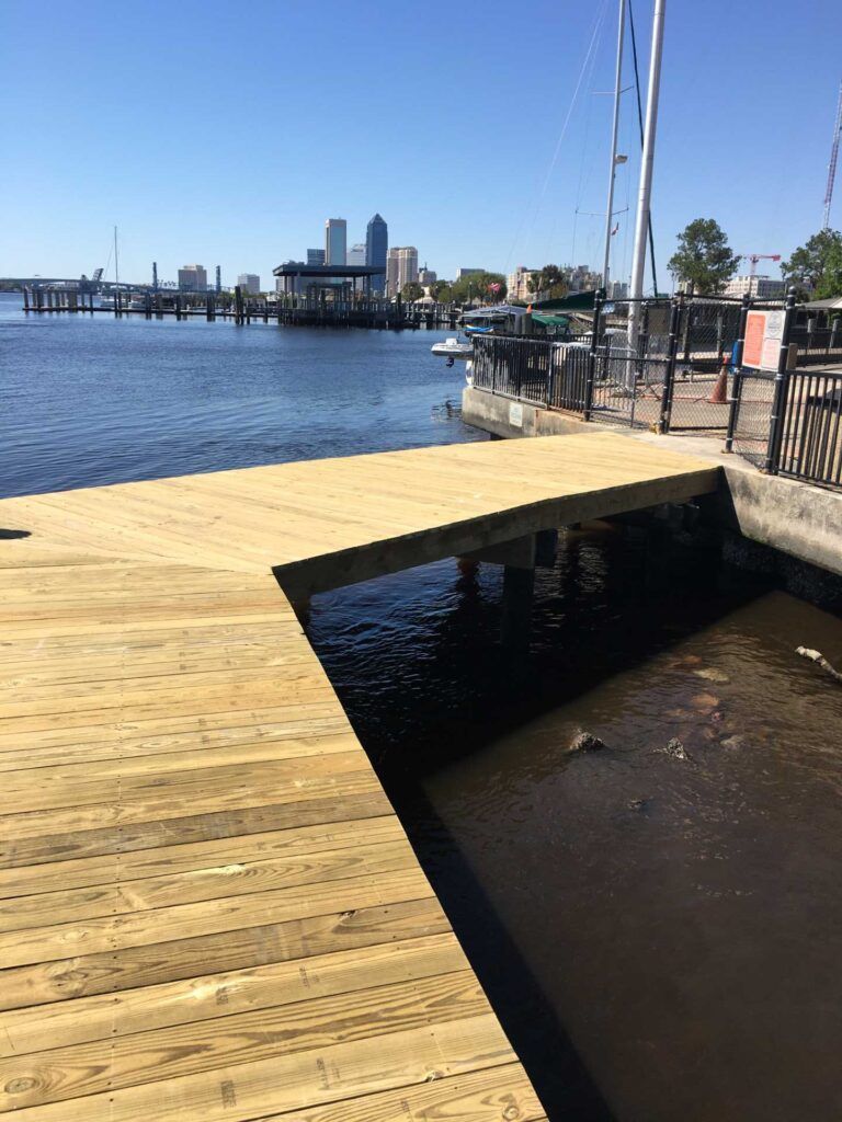 Wooden dock extending into dark water; city skyline in background.
