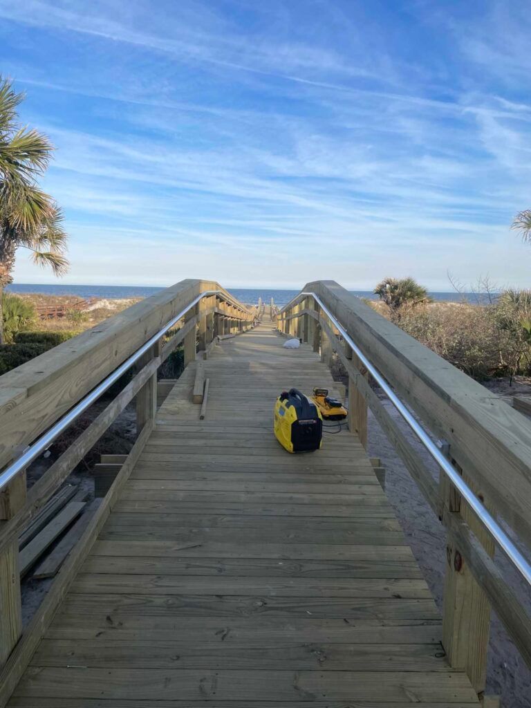 Wooden boardwalk with railings leads to ocean view. A yellow generator sits on the boards.