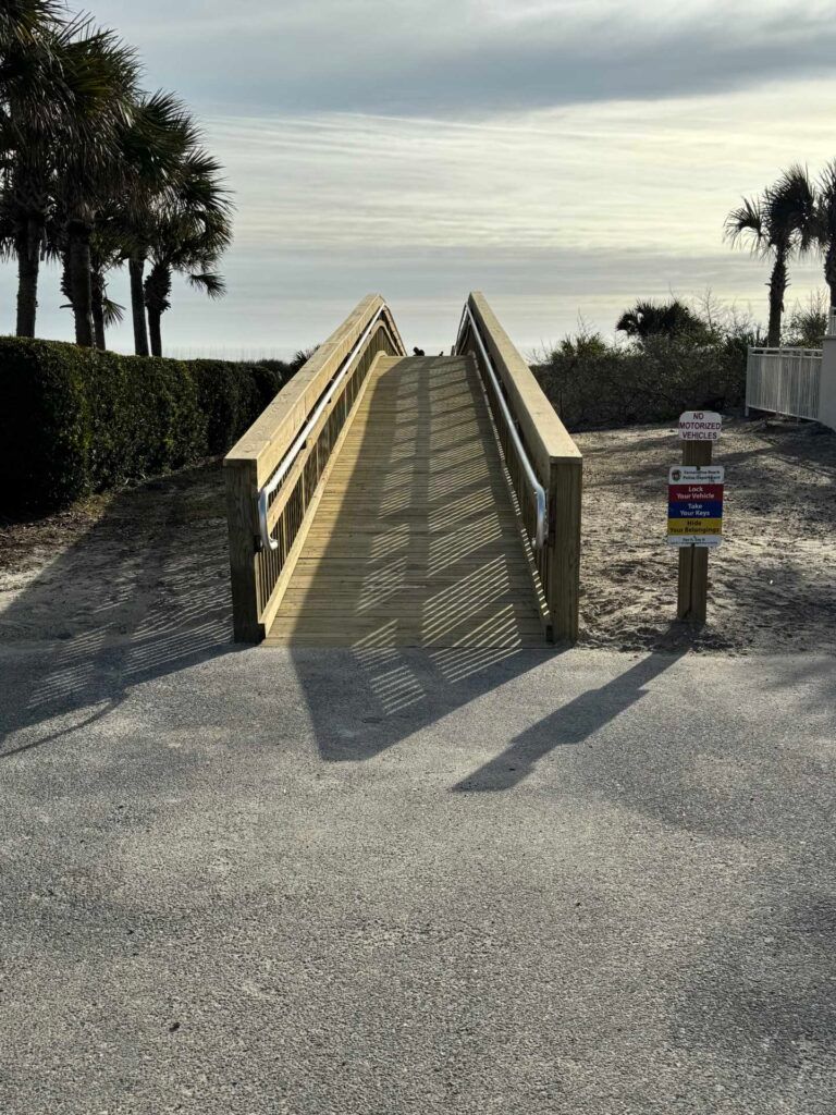 Wooden ramp leading to the beach, gray gravel path, sunny day.