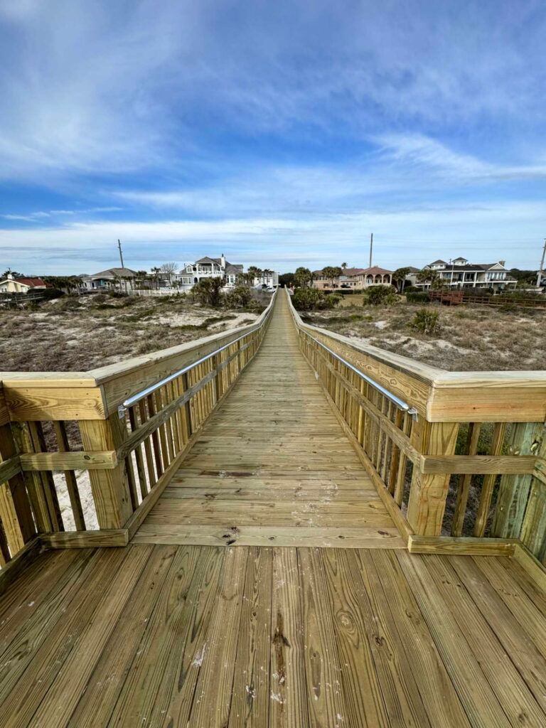Wooden boardwalk leading to beach houses under a blue sky.