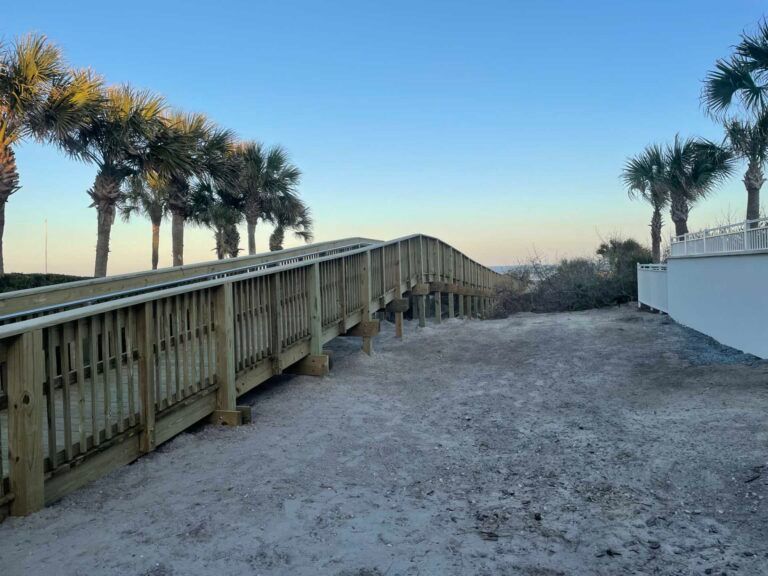 Wooden boardwalk over sandy beach, palm trees line the background.