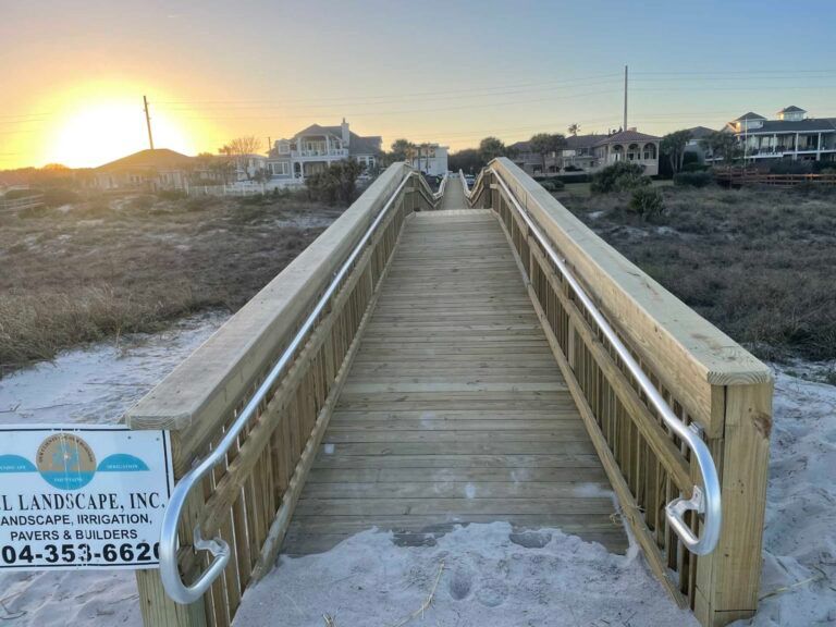 Wooden boardwalk with railings over sand, leading to beach at sunset.