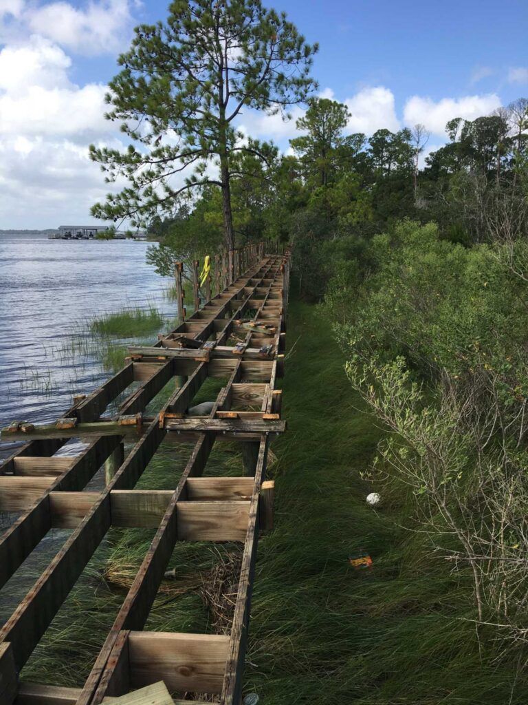 Wooden dock frame along a shoreline. The frame is partially constructed next to a grassy area and water.