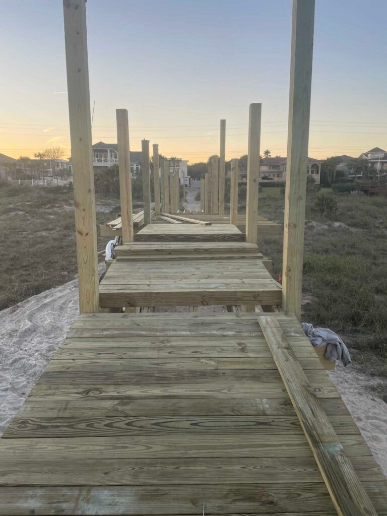 Wooden pier under construction, posts and planks visible, set against a sunset sky.