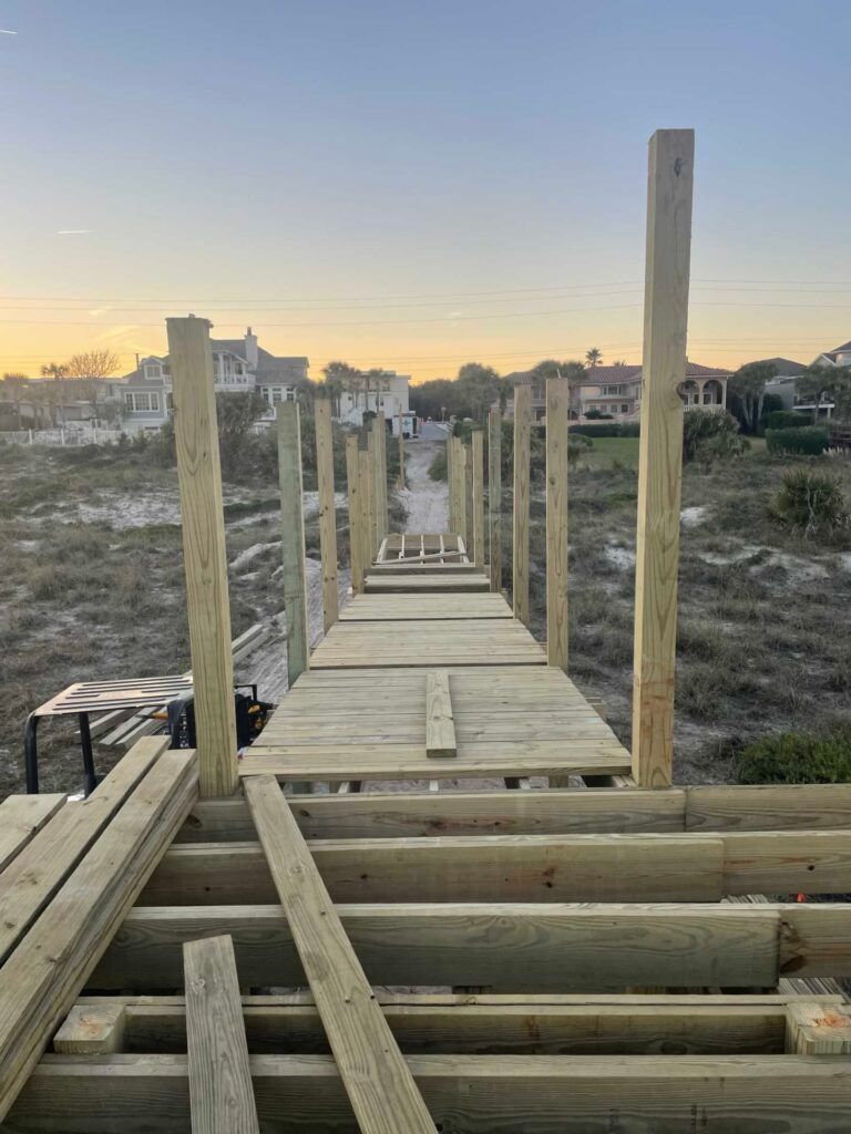 Wooden boardwalk under construction, leading toward buildings, with posts and exposed planks.