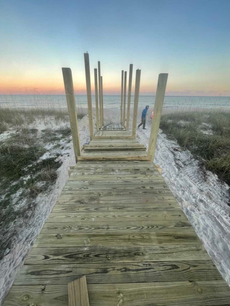 Wooden pier extending to a beach at sunset; person walks at the end of the pier.