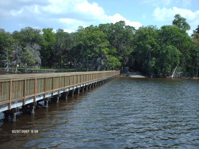 Wooden boardwalk extending over water; trees line the shore.