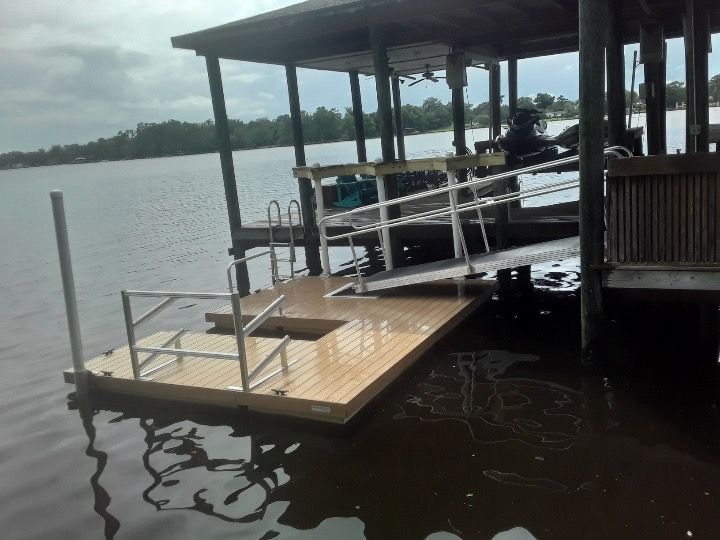 Floating dock with ramp and handrails under a boathouse on a body of water.
