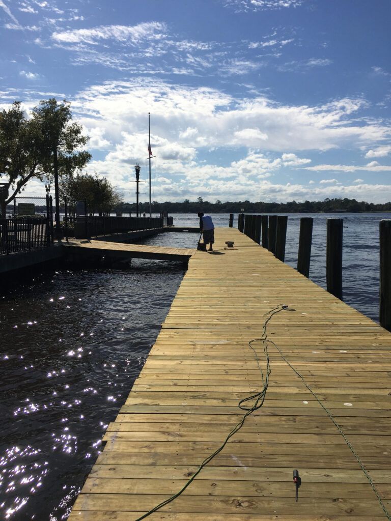Wooden pier extends into water on a sunny day. A person stands at the pier's end.