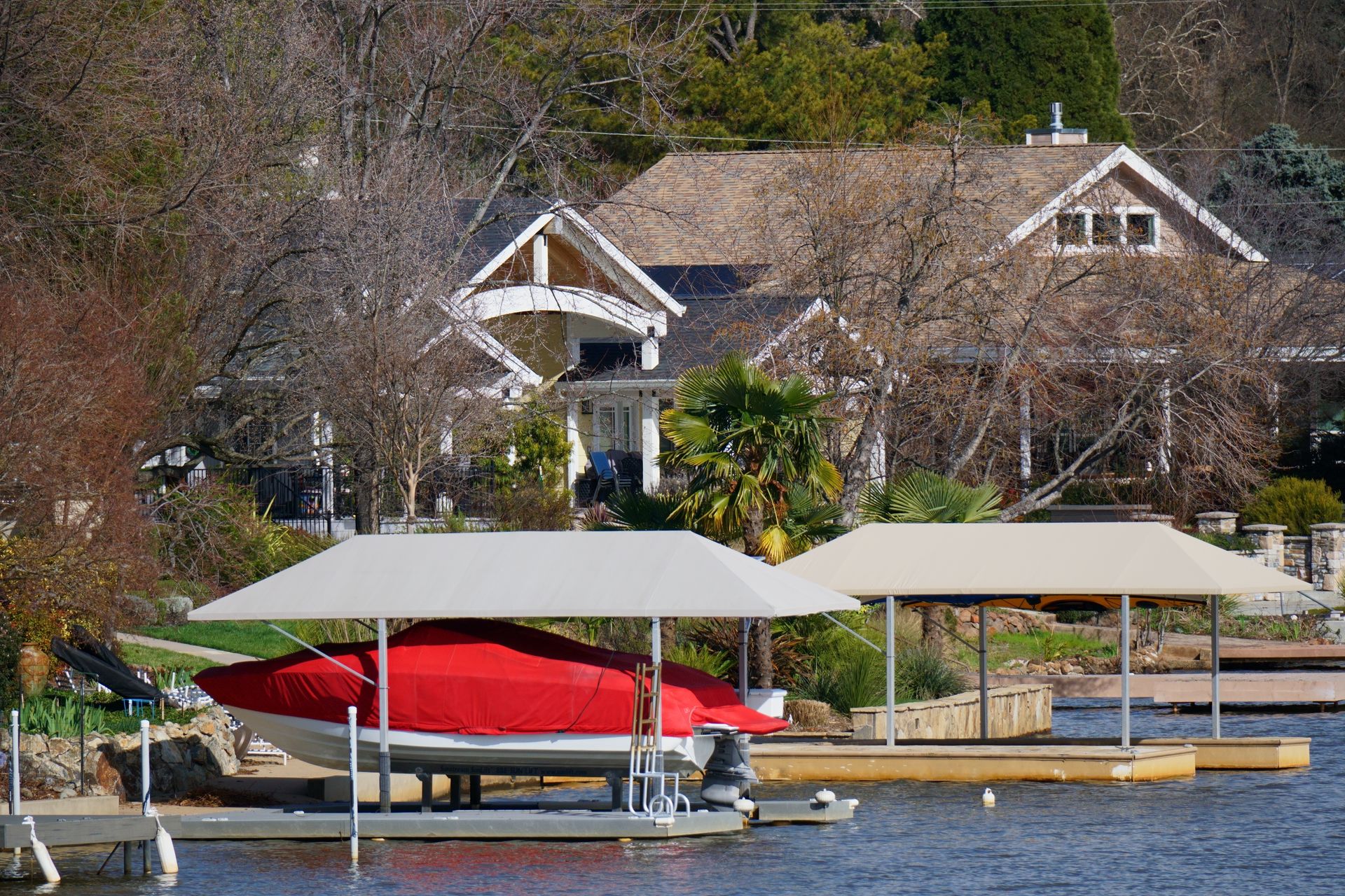 Red boat under dock canopy on a lake with houses and trees in the background