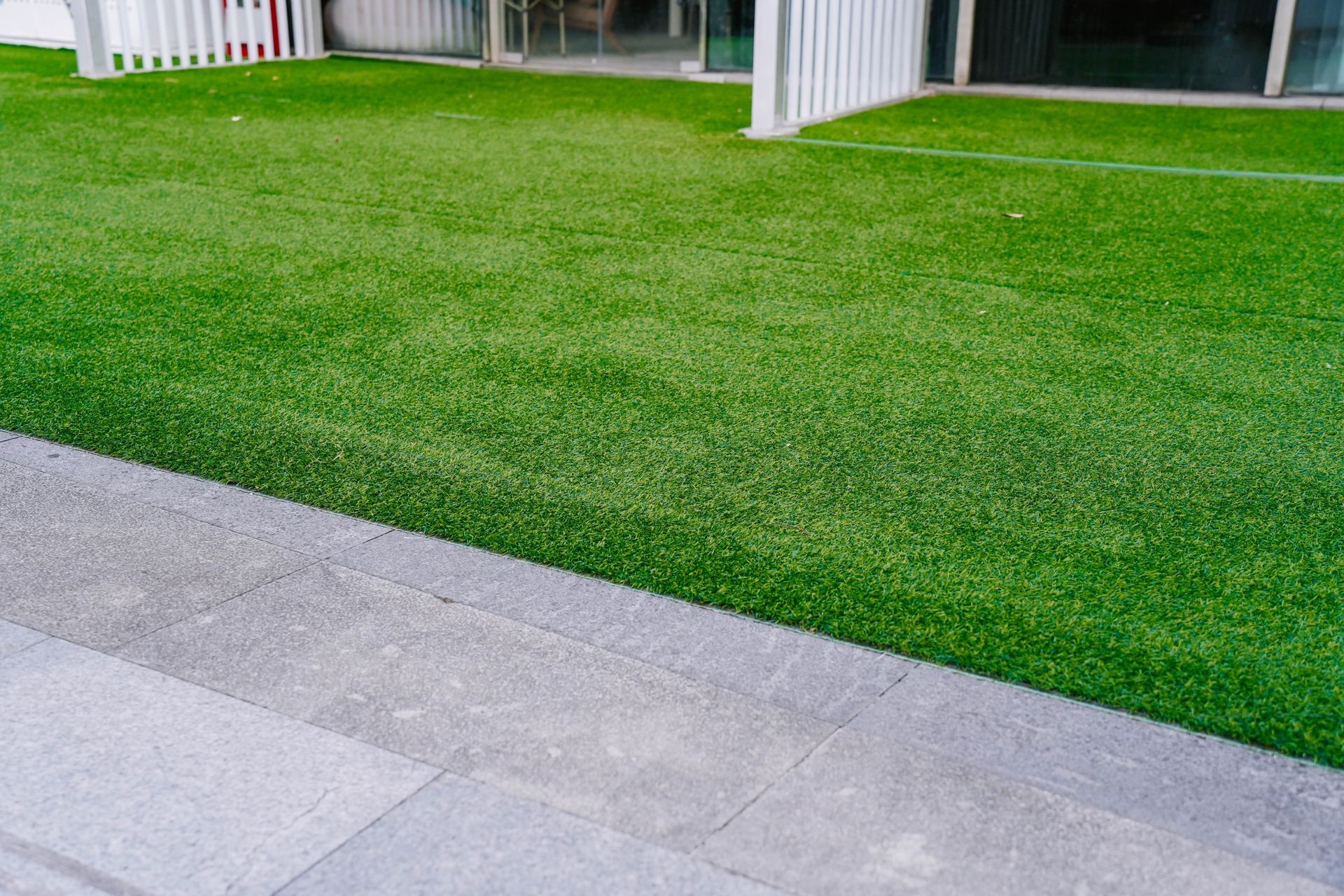 Green artificial turf bordering a gray stone walkway near a building.