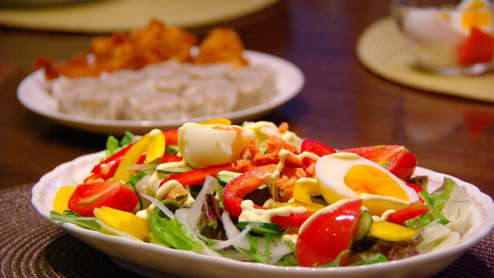 Auf einem Tisch steht ein weißer Teller mit Salat und einem hartgekochten Ei.