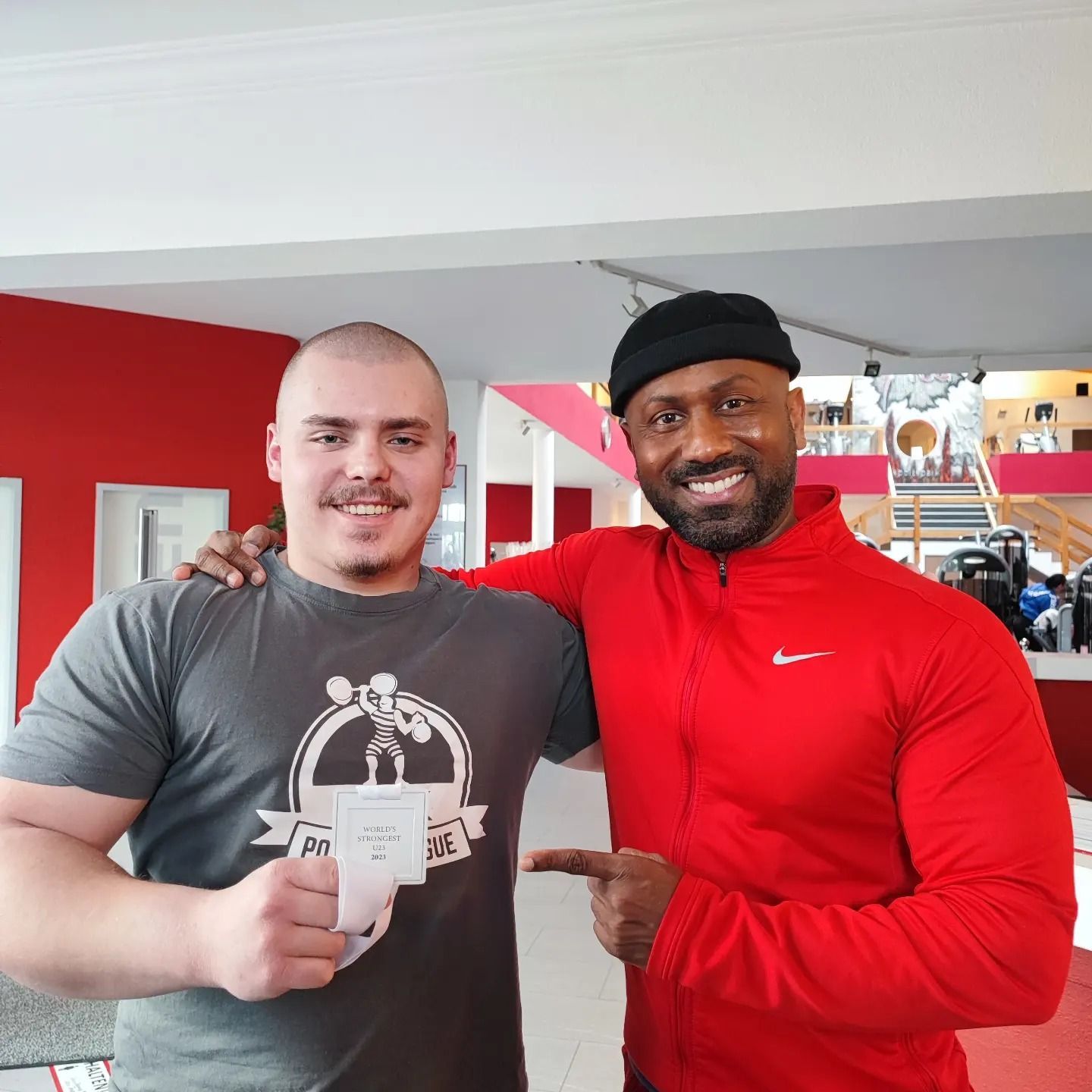 Zwei Männer posieren für ein Foto in einem Fitnessstudio. Einer trägt eine Nike-Jacke.