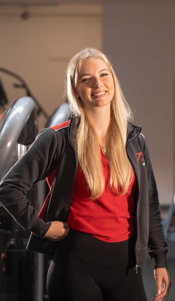 Eine Frau steht mit den Händen auf den Hüften in einem Fitnessstudio.