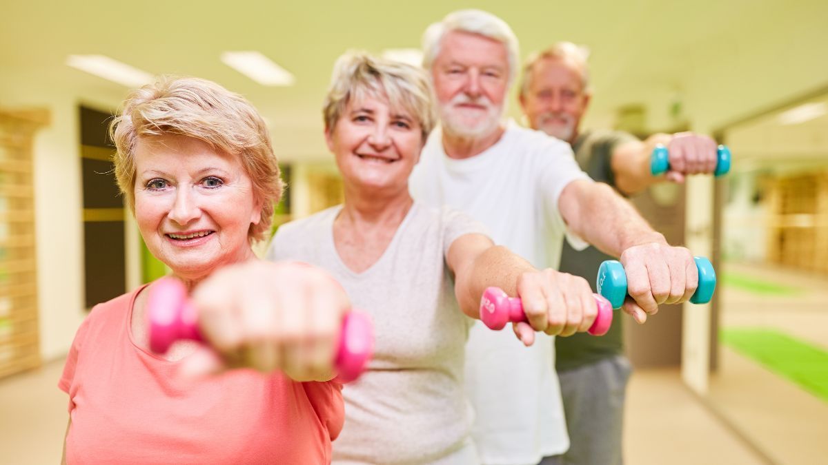 Eine Gruppe älterer Menschen hält in einem Fitnessstudio Hanteln.