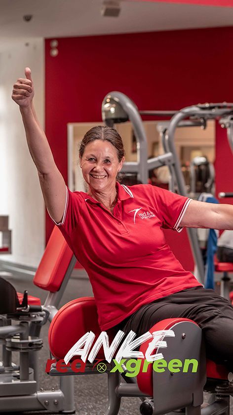 Eine Frau sitzt in einem Fitnessstudio auf einem Gerät und streckt den Daumen nach oben.