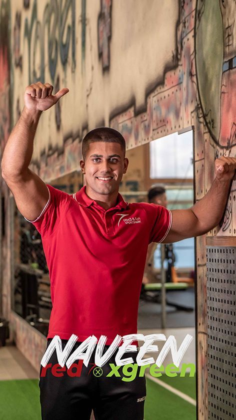 Ein Mann in einem roten Hemd steht in einem Fitnessstudio vor einem Spiegel.
