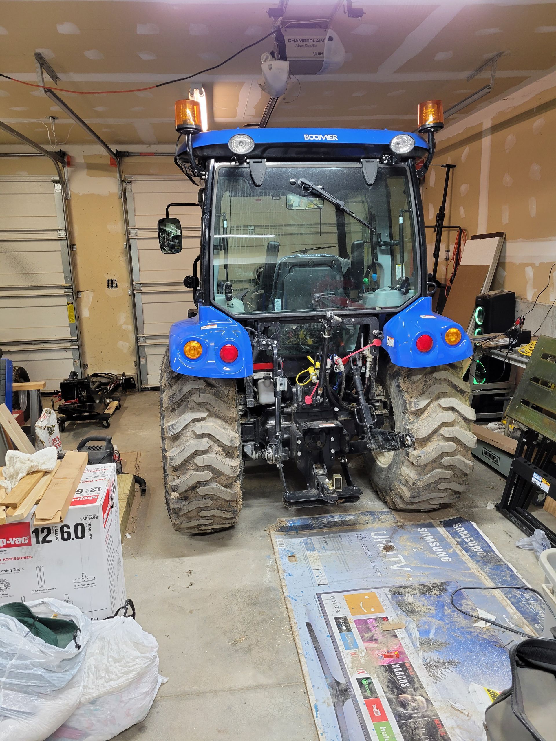 Blue tractor with dirty tires inside a cluttered garage.